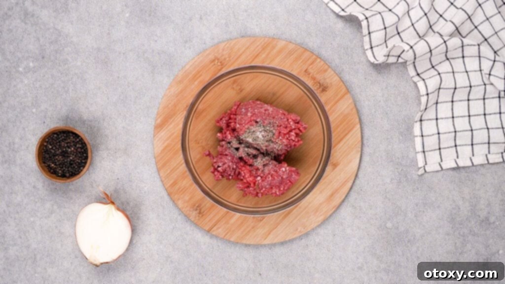 Raw ground beef seasoned with salt and black pepper in a mixing bowl, ready for cooking.