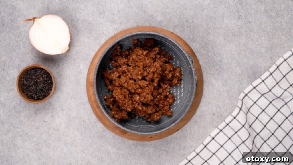 The beef and sauce mixture spread evenly in a greased baking pan, forming the base of the crustless pizza.