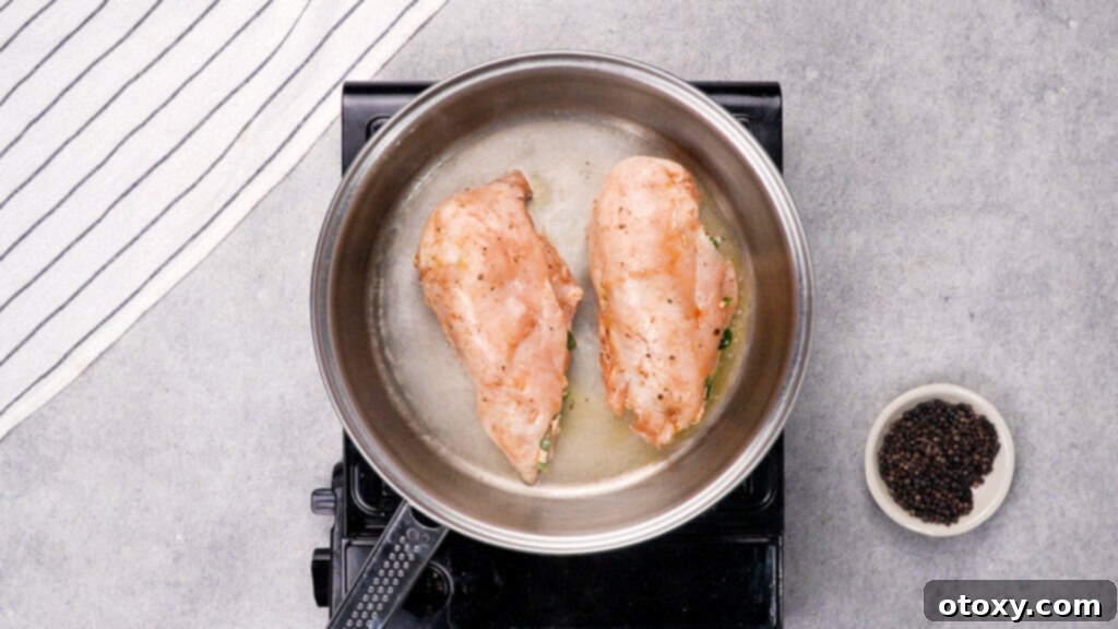 Stuffed chicken breasts searing in a hot skillet with melted butter.