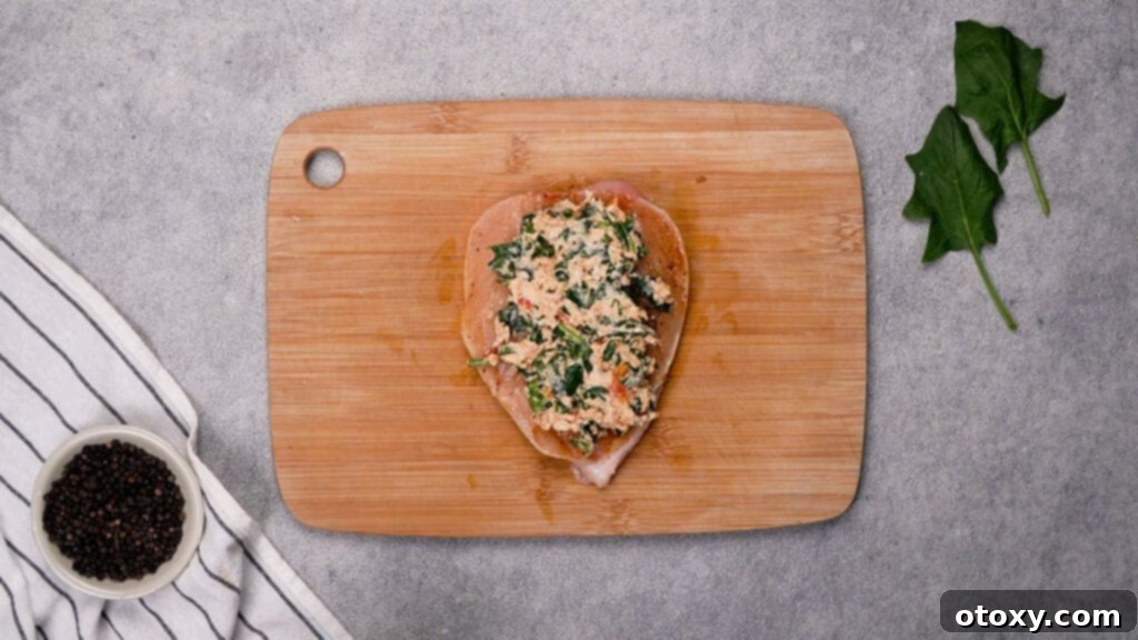 Spoonful of creamy filling inside a butterflied chicken breast, secured with toothpicks.