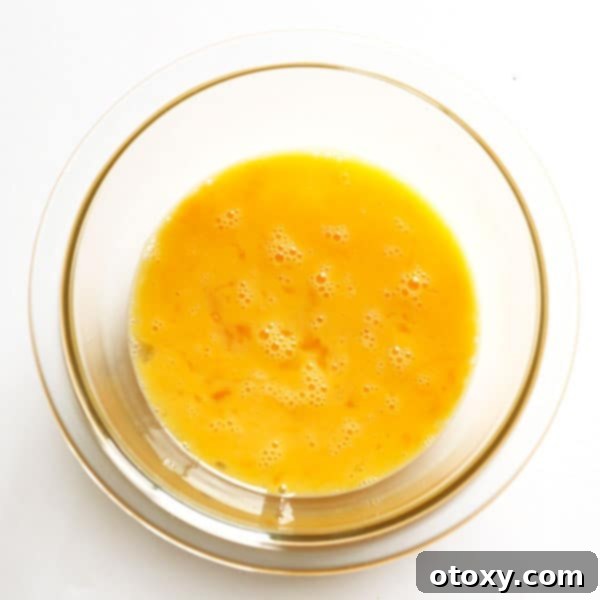 Lightly whisked eggs with a dash of milk in a clear glass bowl, ready for cooking