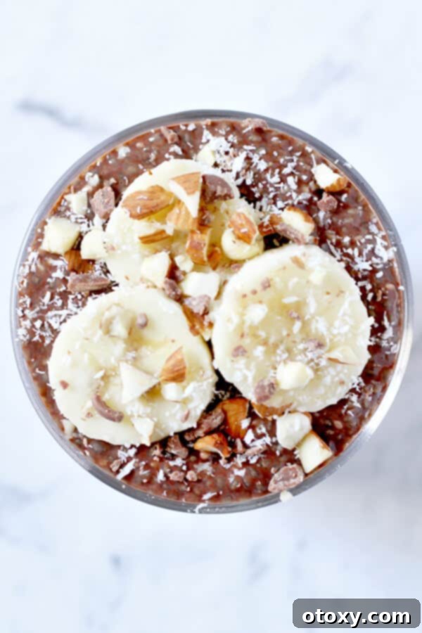 Guilt-Free Chocolate Chia Treat 3 Overhead view of a glass filled with creamy chocolate chia pudding, adorned with vibrant banana slices, finely chopped almonds, and delicate shredded coconut flakes.