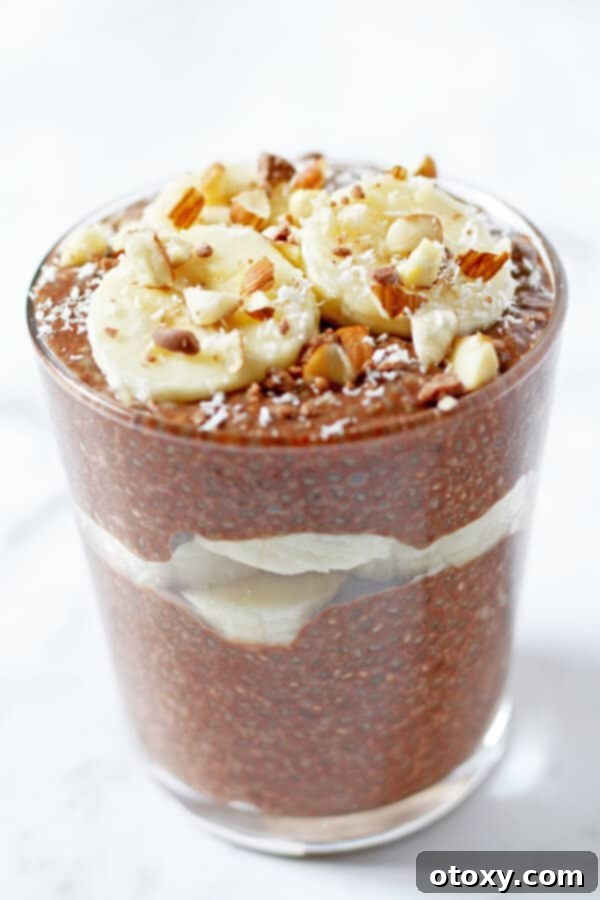 Guilt-Free Chocolate Chia Treat 5 Close-up of a glass filled with chocolate chia pudding, generously topped with fresh banana slices, crunchy chopped almonds, and sweet shredded coconut, creating an inviting visual.