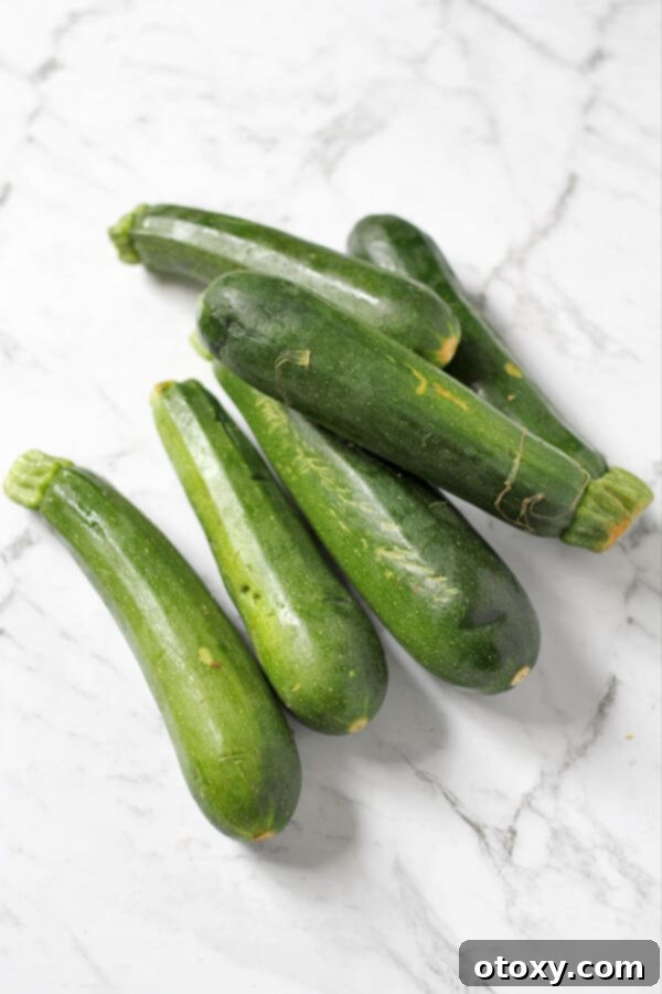 Six fresh zucchinis laid out on a white marble background