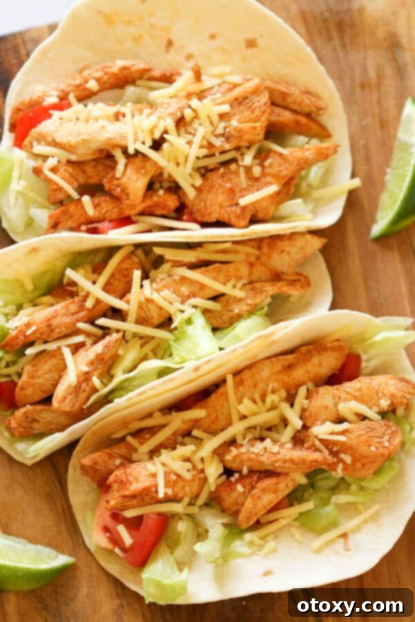 Three healthy chicken tacos on a rustic wooden board, garnished with fresh cilantro and a lime wedge.