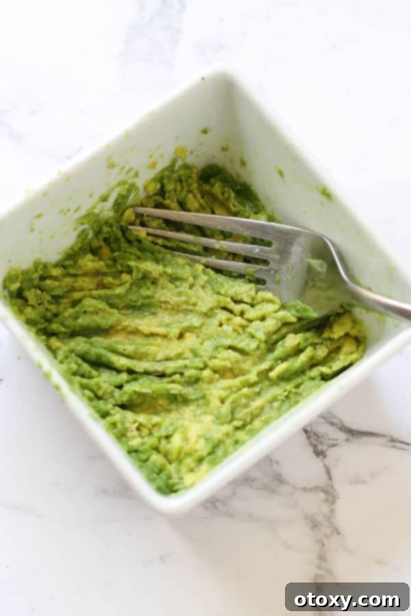 A fork pressing into a bowl of creamy mashed avocado, ready for taco topping.