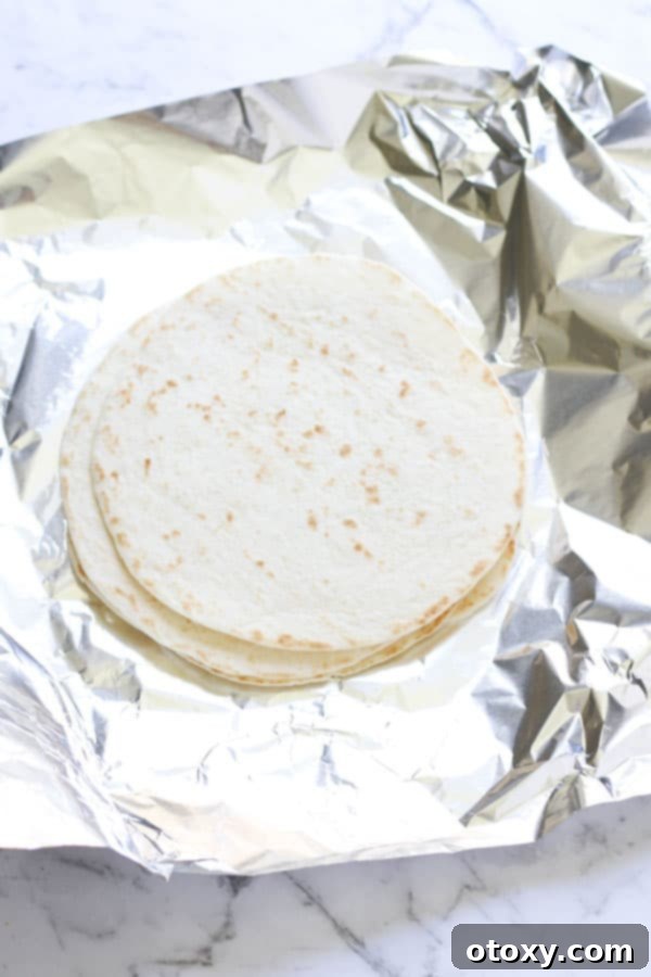 A stack of mini flour tortillas on aluminum foil, ready to be warmed for tacos.
