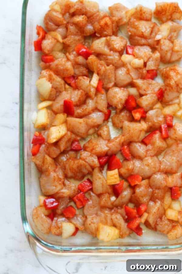 Diced raw chicken, bell pepper, and onion pieces seasoned on a baking tray, ready for the oven.