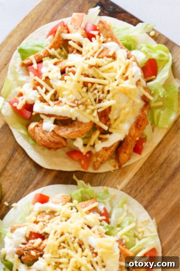 Two vibrant chicken tacos on a rustic wooden cutting board, showcasing the colorful filling and fresh garnishes.