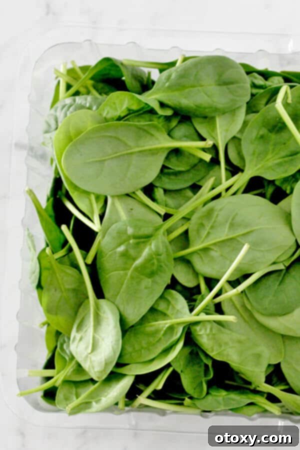 Fresh, vibrant green spinach leaves loosely packed in a clear plastic container, ready to be added to a healthy soup recipe.