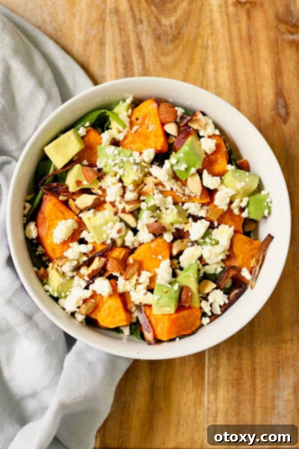 Delicious Roasted Sweet Potato, Avocado, and Feta Salad served in a white bowl on a rustic wooden cutting board, garnished with fresh herbs and almonds.