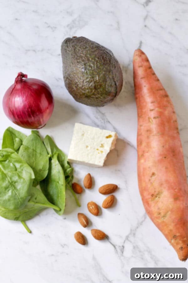 Fresh ingredients for Roasted Sweet Potato and Feta Salad, including diced sweet potatoes, sliced avocado, crumbled feta, fresh spinach, red onion, almonds, and honey lemon vinaigrette components, beautifully arranged on a marble background.