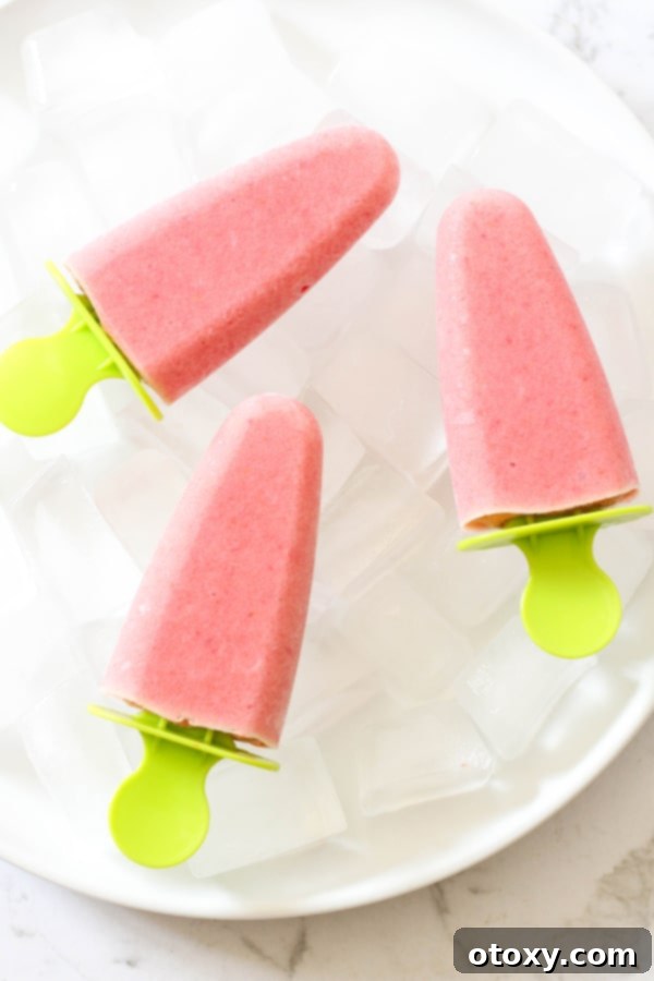 3 strawberry pineapple popsicles on a plate filled with ice cubes, showcasing their vibrant colors and refreshing appeal.
