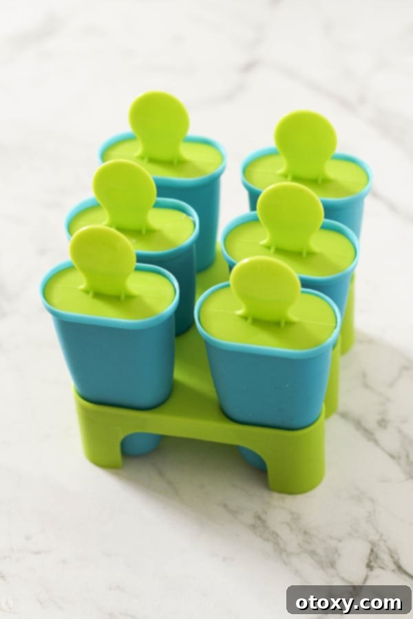 An array of empty popsicle molds arranged neatly on a pristine white marble background, ready to be filled with the delicious mixture, symbolizing the anticipation of homemade frozen treats.