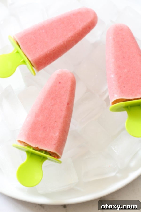 Three perfectly crafted strawberry pineapple popsicles nestled on a plate filled with ice cubes, highlighting their refreshing appeal and readiness to be enjoyed.