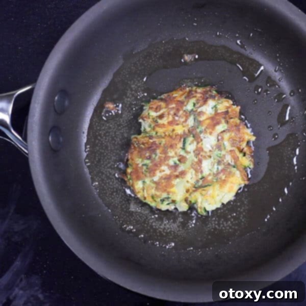 Healthy Zucchini Fritters: Gluten-Free, Paleo and Whole30 9 A fritter sizzling and cooking in a black skillet pan
