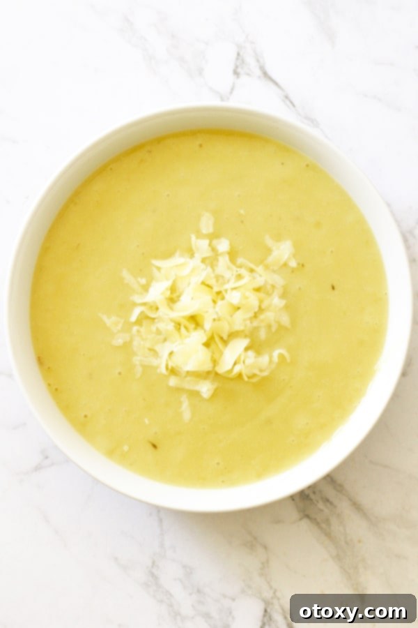 Potato and Leek Soup in a white bowl topped with shredded cheddar cheese, ready to be enjoyed.