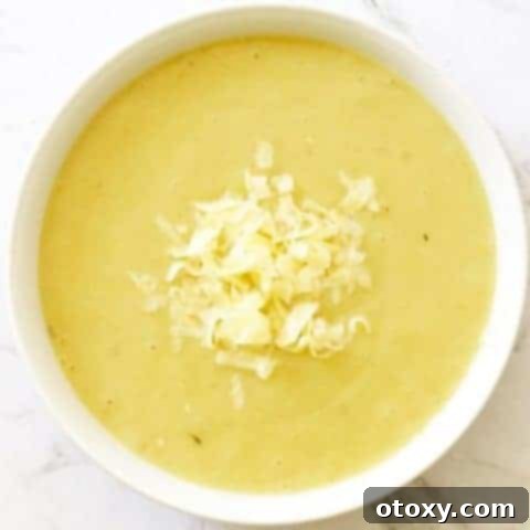 Creamy Potato and Leek Soup in a white bowl topped with shredded cheddar cheese.