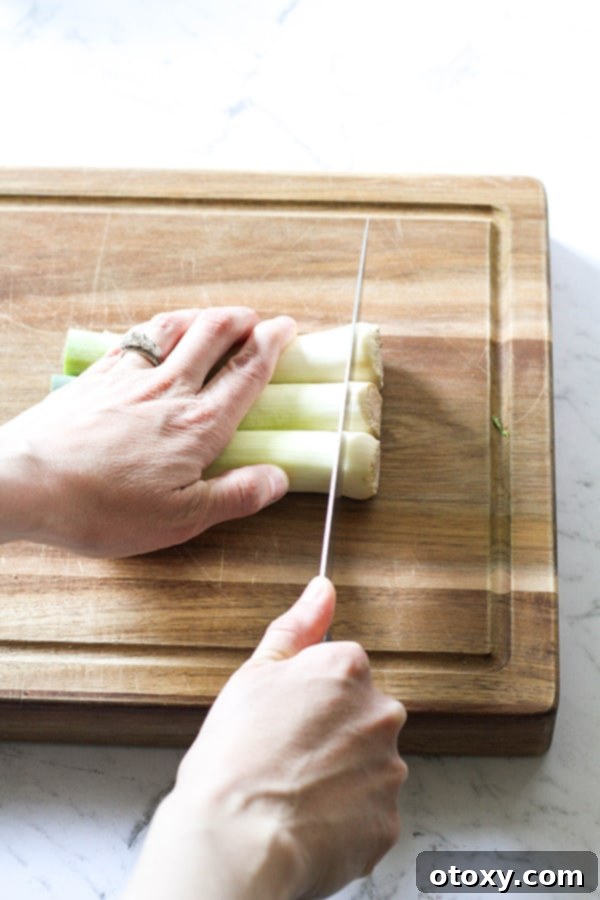 Leeks on a wooden chopping board with a hand carefully slicing off the root ends.