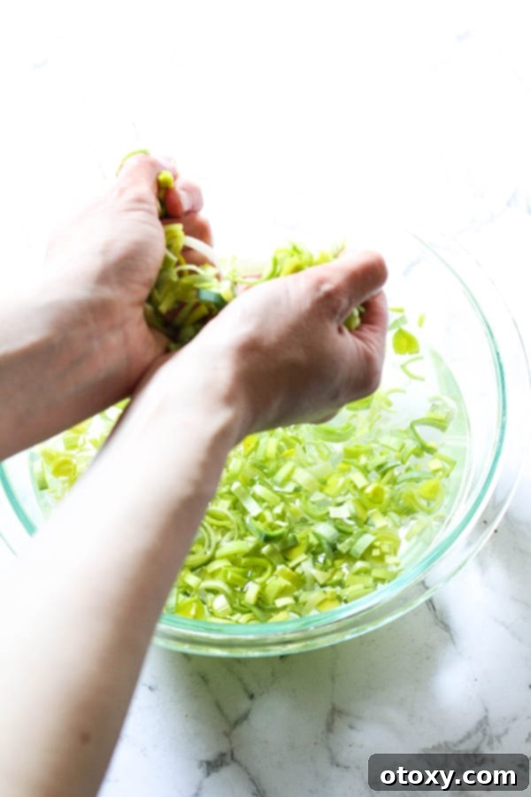 Hands gently removing handfuls of clean sliced leeks from a mixing bowl filled with water, allowing dirt to settle.
