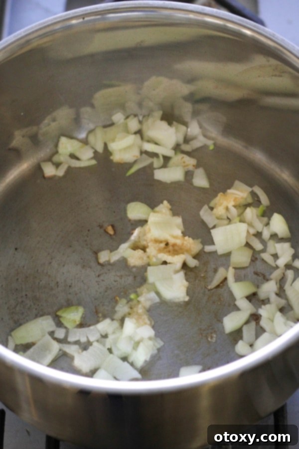 Diced onion and crushed garlic gently sautéing in olive oil in a large saucepan, forming the aromatic base of the soup.