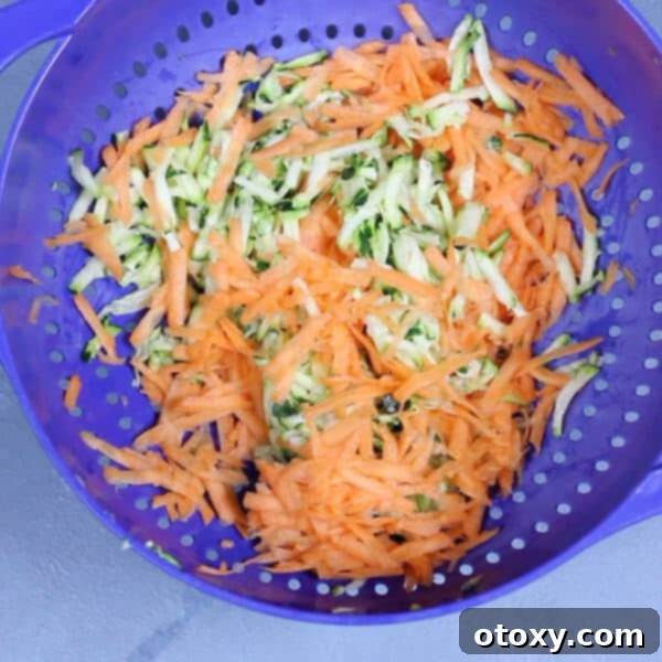 Shredded carrot and zucchini resting in a colander after being salted, preparing for moisture removal.