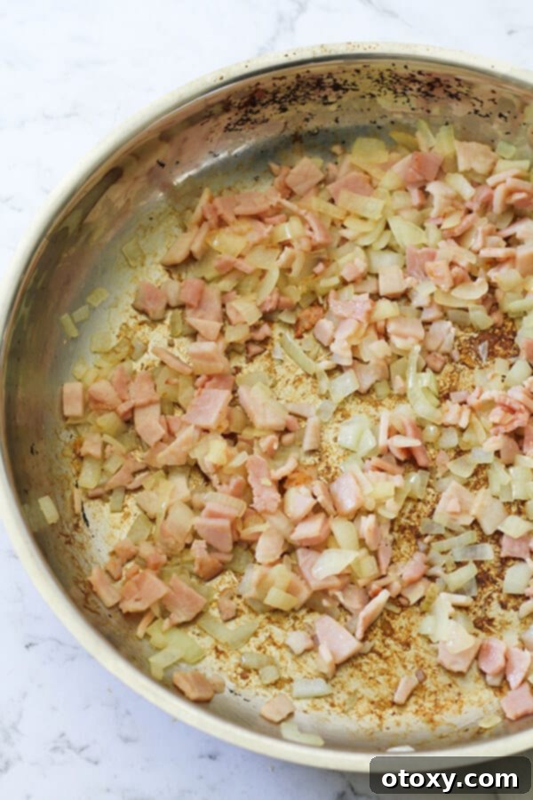 Diced bacon and chopped onion sizzling in a frying pan, cooking to golden perfection.