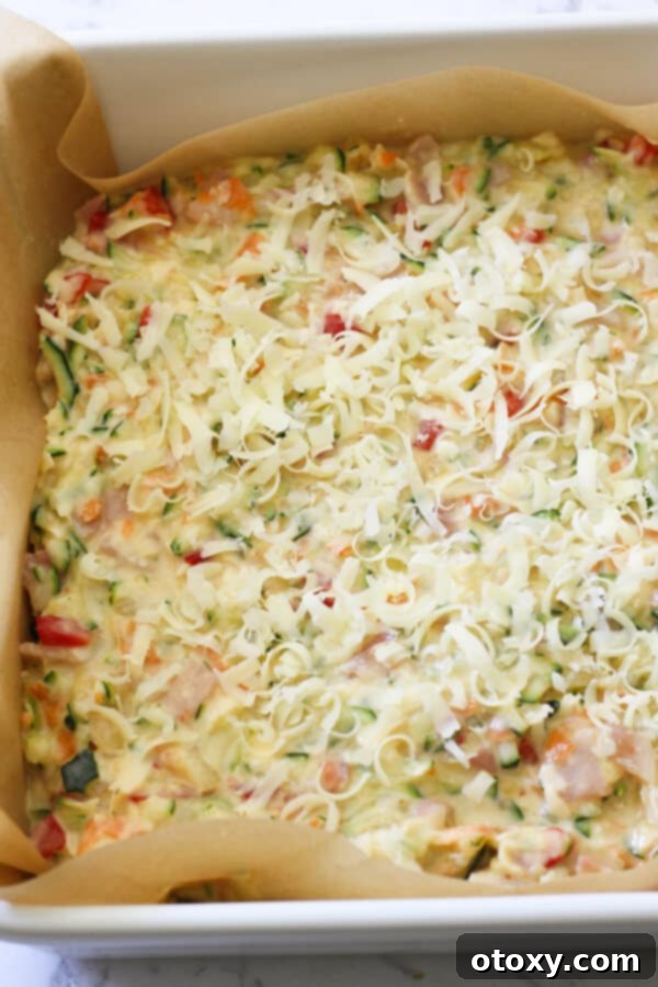 Zucchini and Bacon Slice mixture in a baking tray, topped with cheese and ready to go into the oven.