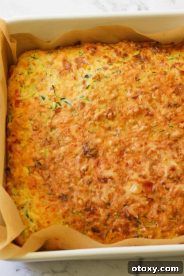 Freshly baked Zucchini and Bacon Slice in a baking tray, golden and bubbling, just out of the oven.