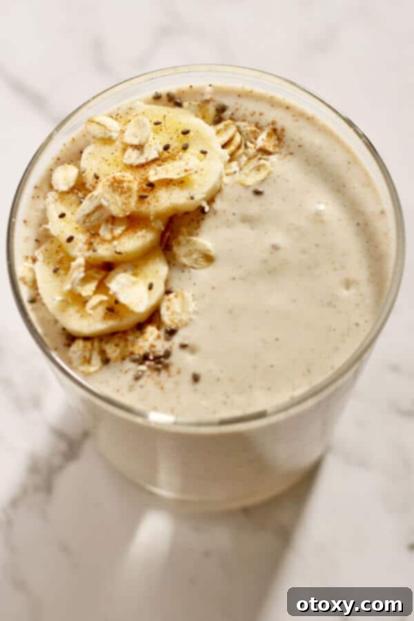 A vibrant banana oat smoothie in a clear glass, beautifully garnished with fresh banana slices, a sprinkle of cinnamon, whole rolled oats, and tiny chia seeds, emphasizing its healthy and hearty appeal.