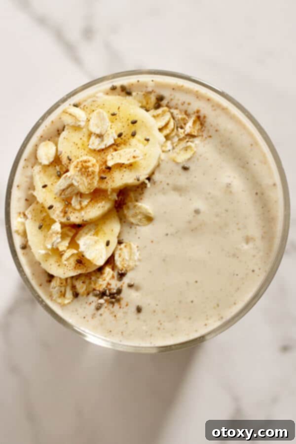 A close-up, top-down view of a banana oat smoothie, beautifully garnished with slices of fresh banana, scattered rolled oats, a dusting of cinnamon, and a sprinkle of chia seeds, highlighting its wholesome ingredients.