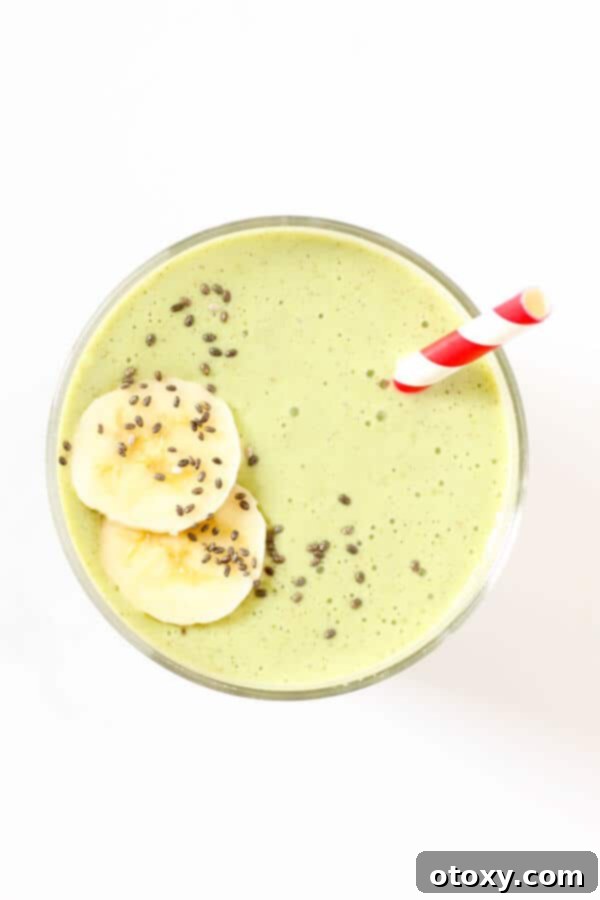 spinach mango smoothie in glass with red straw and banana slices on top