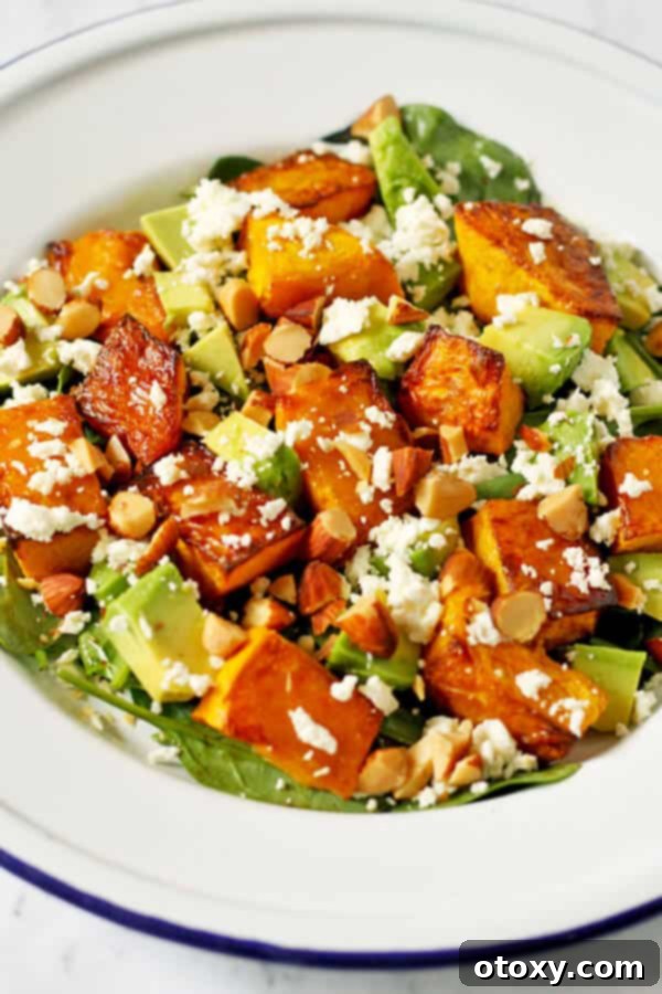 A generous serving of roast pumpkin, spinach, and feta salad on a pristine white plate, garnished with nuts