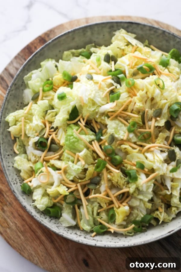 A large bowl of cabbage and crunchy noodle salad resting on a wooden board.