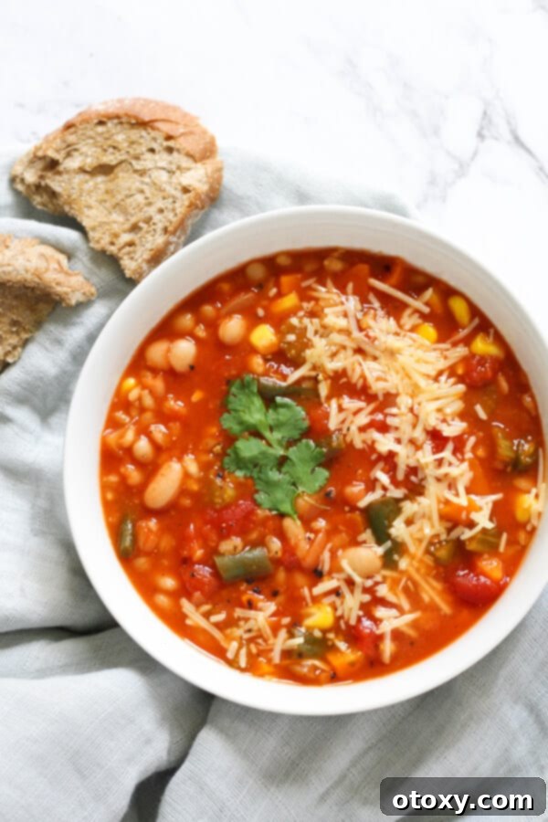 a bowl of vegetable barley soup on a grey napkin with crusty bread