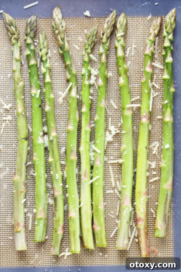 raw asparagus spears laid out in a single layer on a baking tray covered in parmesan cheese and minced garlic