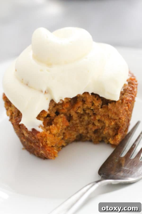 carrot cupcake on a white plate with a bite removed.