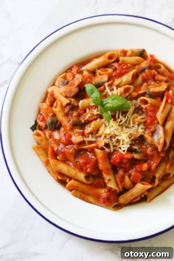 A delectable serving of Bacon and Mushroom Pasta on a white plate, garnished with fresh basil leaves and a sprinkle of grated Parmesan cheese.