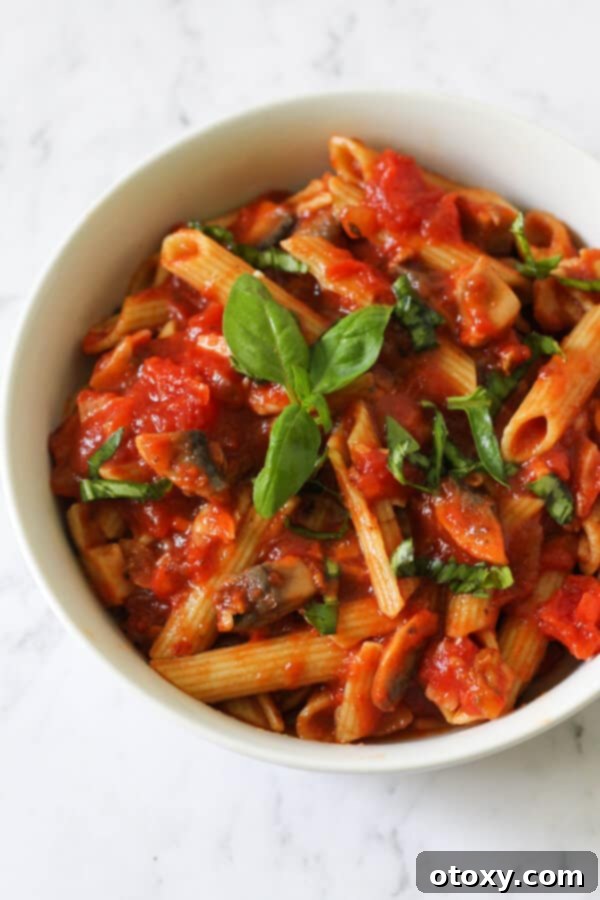 A close-up of Bacon and Mushroom Pasta served in a white bowl, generously topped with fresh green basil leaves for garnish.