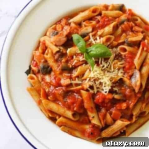 A beautifully plated serving of Bacon and Mushroom Pasta, garnished with fresh basil and a generous dusting of Parmesan cheese.