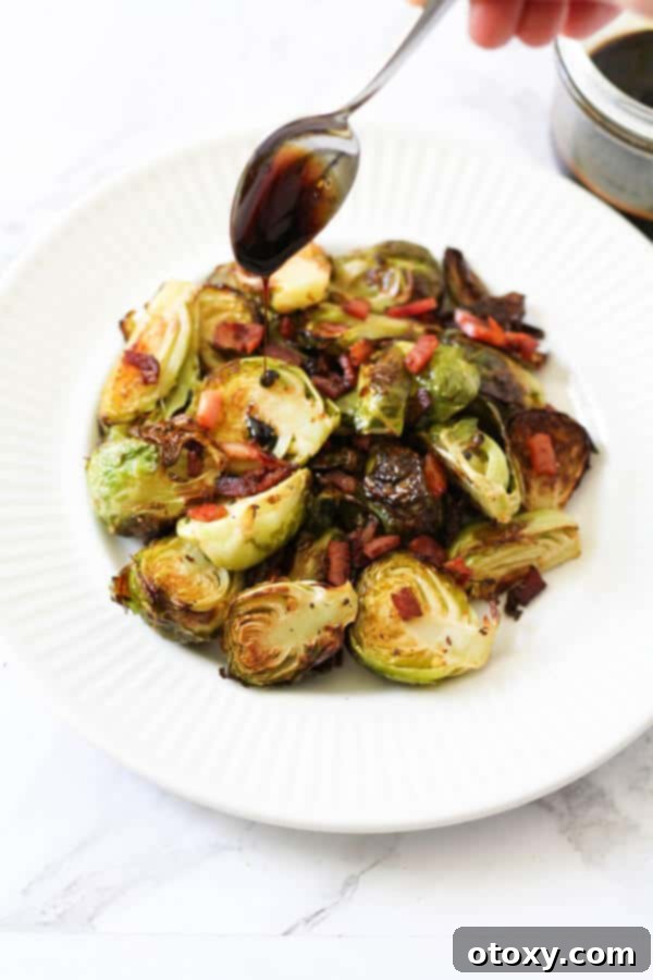 a spoon held above a plate of roasted brussels sprouts drizzling balsamic glaze over the vegetables