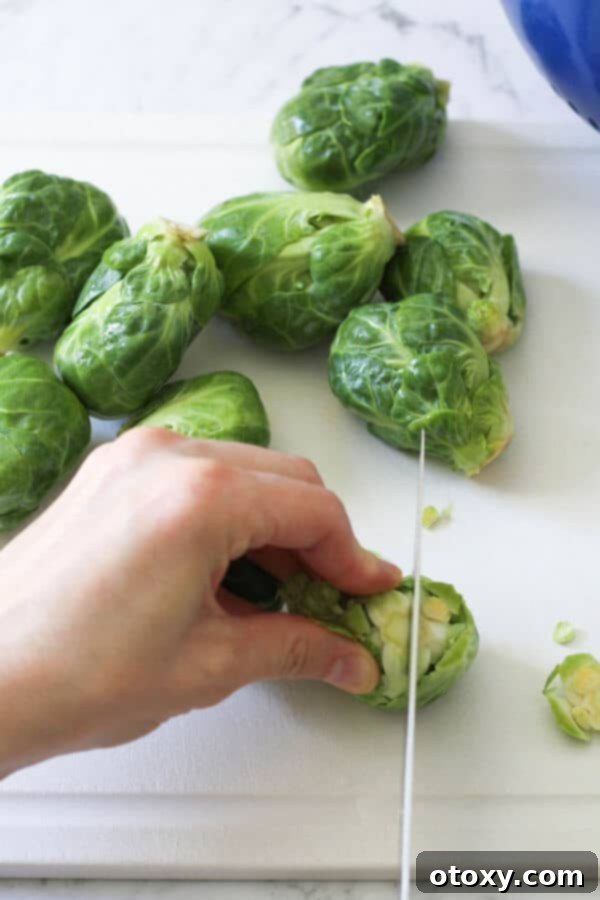 a hand demonstrating how to cut brussels sprouts in half with a knife