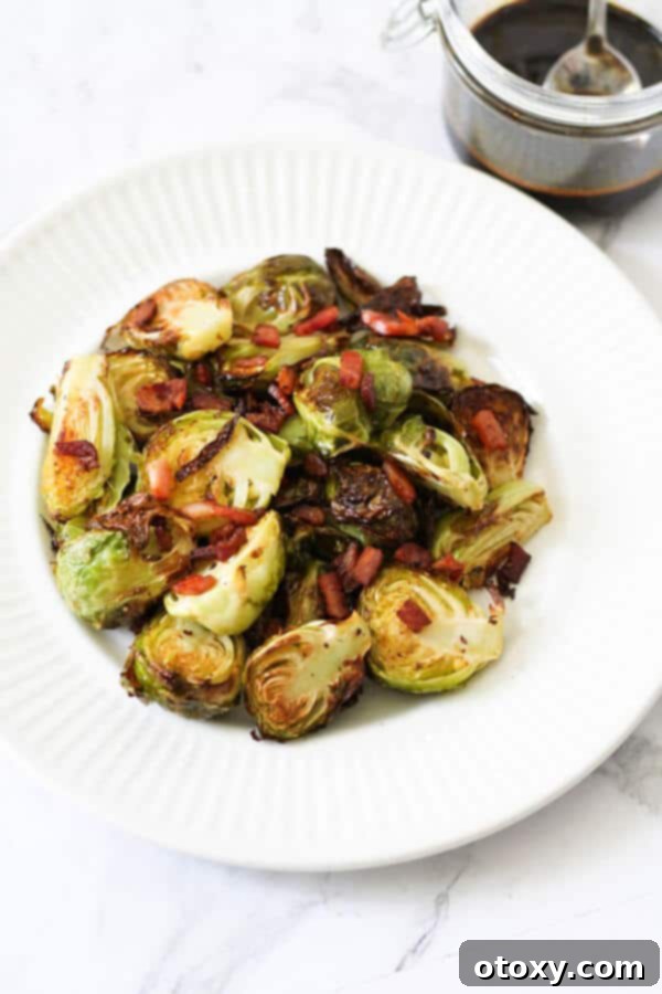 roasted brussels sprouts with bacon on a white plate with a jar of balsamic glaze in the background
