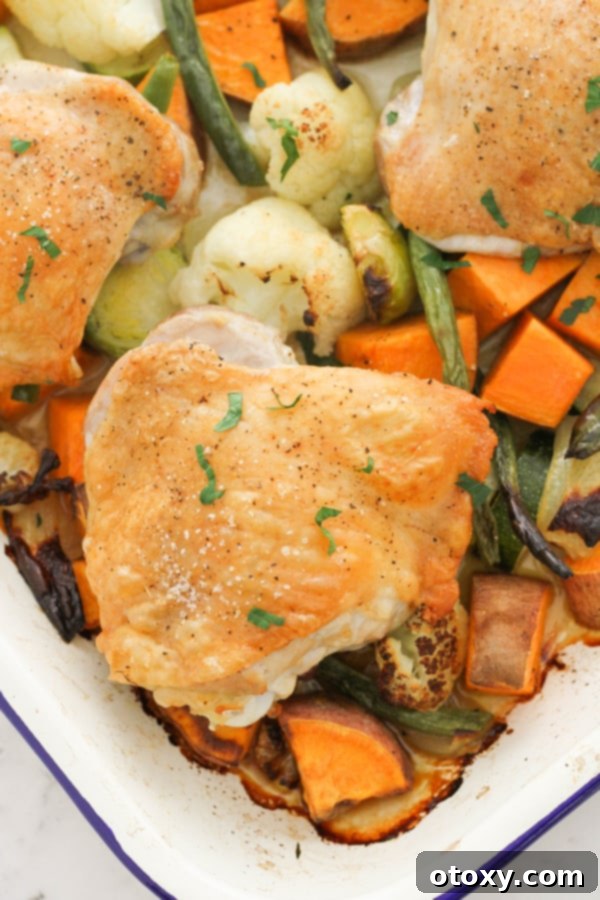 Sheet Pan Golden Chicken Thighs with Roasted Vegetables 2 Golden brown crispy chicken thighs resting on a bed of roasted mixed vegetables on a baking tray, ready to be served. The vegetables include broccoli, carrots, and sweet potatoes.