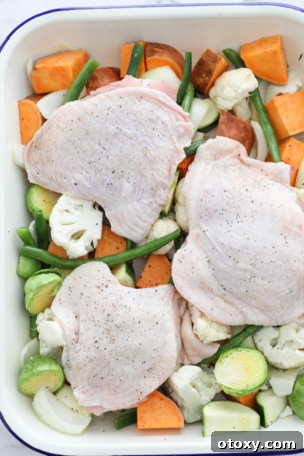 Sheet Pan Golden Chicken Thighs with Roasted Vegetables 8 Chicken thighs, skin side up and perfectly seasoned, arranged on a bed of mixed vegetables on a baking sheet, ready to go into the oven.