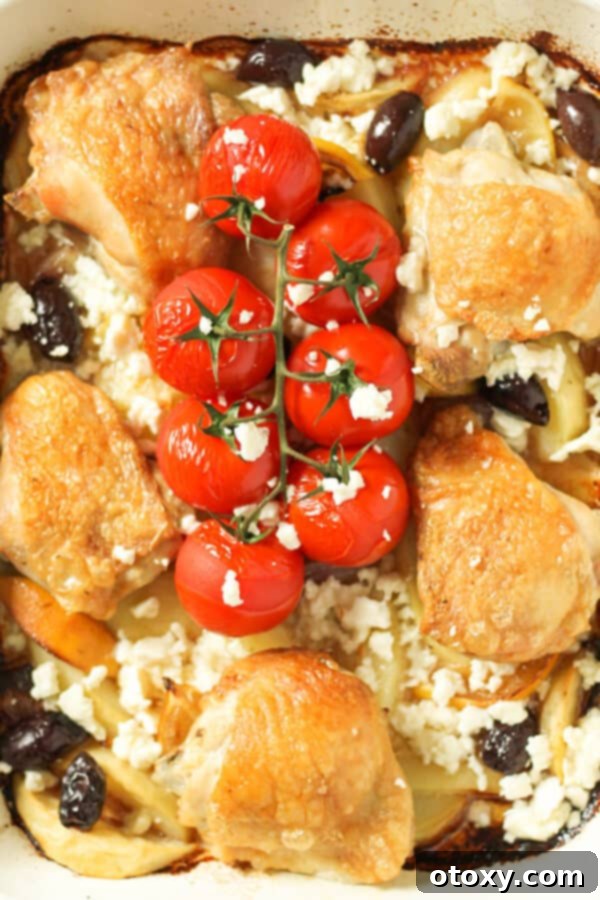 Cooked Greek chicken thighs with lemon potatoes, feta, olives, and cherry tomatoes in a white baking sheet, ready to serve.