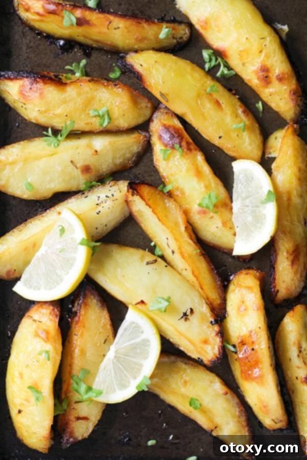 Hellenic Lemon Herb Roasted Potatoes 2 Greek lemon potatoes on a baking tray with fresh lemon slices and a sprinkle of parsley.