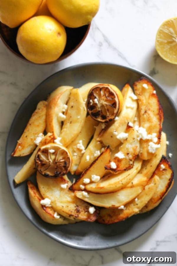 Hellenic Lemon Herb Roasted Potatoes 5 A serving of Greek lemon potatoes on a grey plate, generously topped with crumbled feta cheese.
