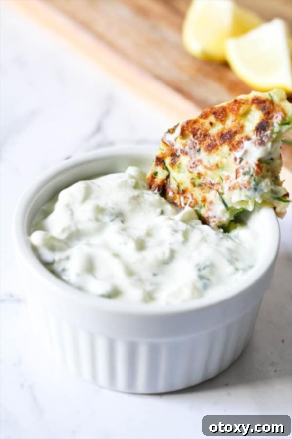 Greek Tzatziki dip in a white bowl with a fritter partially submerged