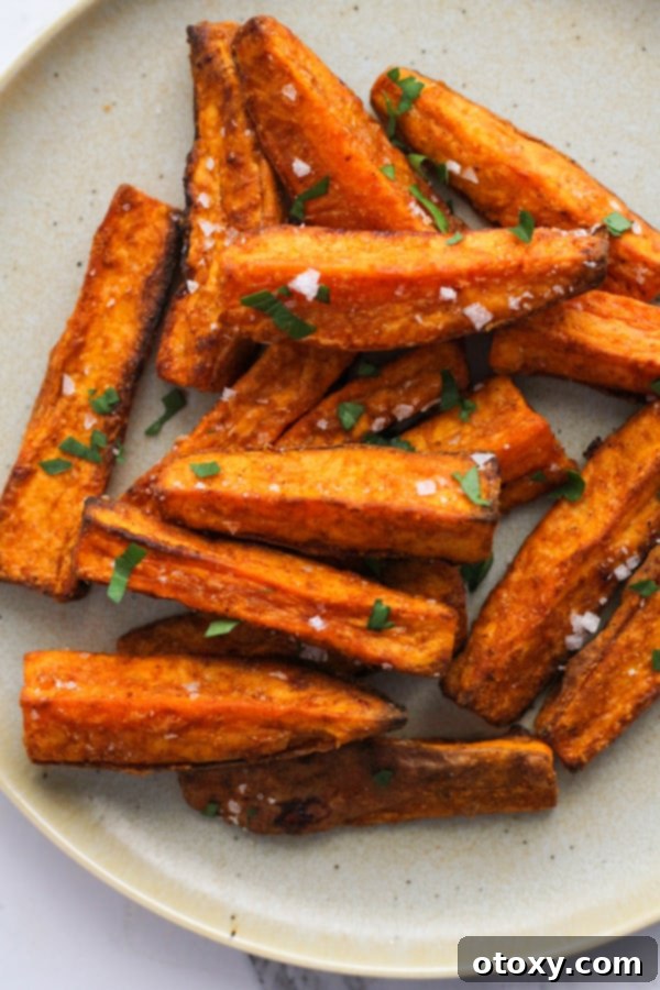 A serving of perfectly air-fried sweet potato wedges, generously seasoned with salt on a white plate.